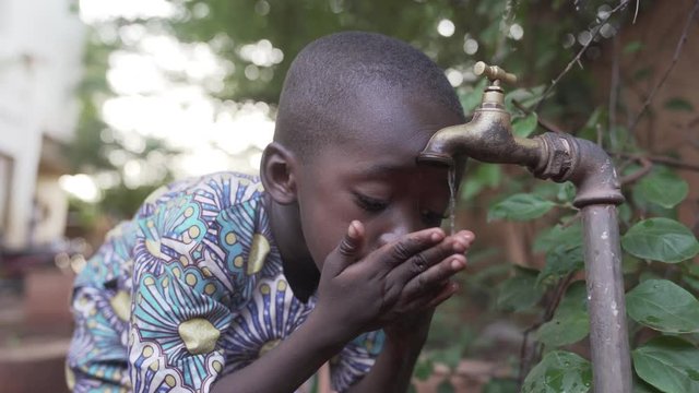 Gorgeous African child drinks fresh water outdoors. 4K RAW clip, please modify and edit (color grade, stabilize, etc.) in postproduction.