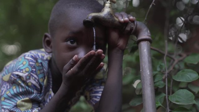 Handsome African boy drinking clean, fresh water from a tap just outside Bamako, Mali in a rural tribal village. 4K RAW clip, please modify and edit (color grade, stabilize, etc.) in postproduction.