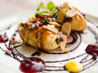 Danish pastry with syrup and sprinkle with almonds and chocolate balls. Put on a white plate with jam around.