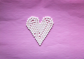 white pills laid out in the shape of a heart on a pink background. concept - heart disease, heart disorders and drugs, cardiology.