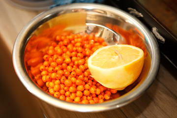Orange berries of sea buckthorn and lemon in a metal plate. Healthy food. Natural vitamins. Ingredients for the preparation of homemade pastes