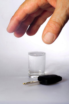 The concept of danger of driving under the influence of alcohol - a glass of alcohol, car keys and a hand reaching for a glass