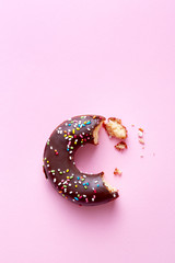 Half eaten donut with chocolate coating and sprinkles on a pink background viewed from above. Sweet food leftovers. Top view. Copy space