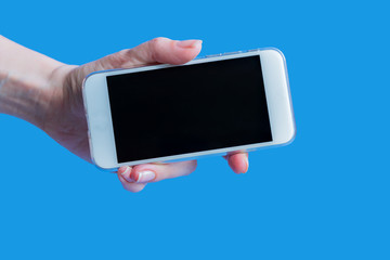 white mobile phone in left female's hand on blue background with copy space