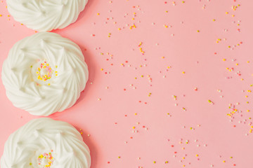 top view of homemade white air meringues and confectionery decorations on pink background