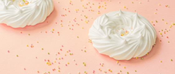  homemade white air meringues and confectionery decorations on pink background, banner