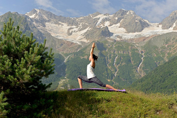 Young athletic woman doing yoga on the background of snow-capped mountains.