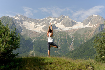 Young athletic woman doing yoga on the background of snow-capped mountains.