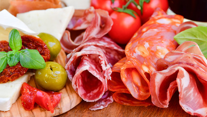 Traditional italian antipasto with prosciutto, parmesan cheese and brie cheese, sun-dried tomatoes, salami, green olives and Basil, wooden table, Italian restaurant, selective focus