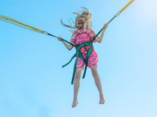 The girl in the dress flies up with the help of stretching straps against the blue sky.