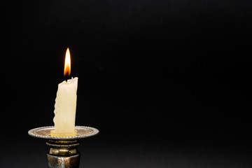 Lighted candle in an old candlestick on a black background