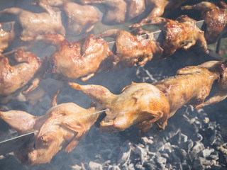 A lot of grilled chicken is roasted on a spit in the smoke.
