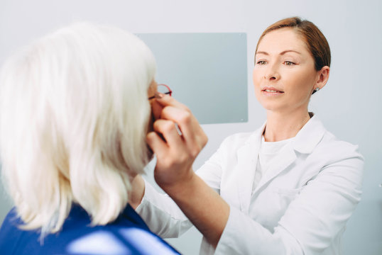 Optomerist is putting new glasses on matue woman face
