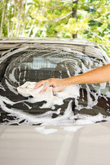 Man washing car at home. Closeup man hand use cloth washing window of silver car.