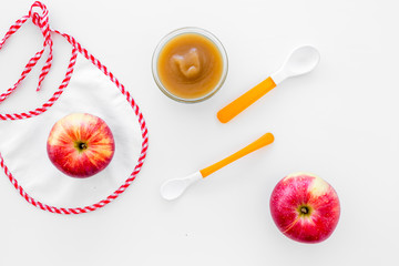 Baby food concept. Apple puree in bowl near bib, apple, spoon on white background top view