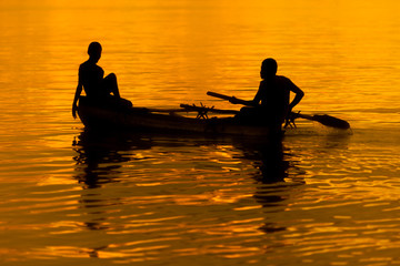 Two people in a small boat at orange and golden sunset