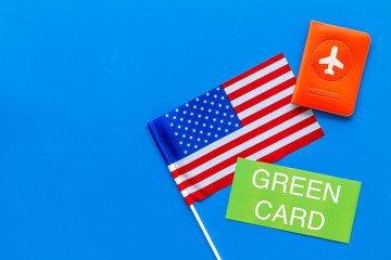 Green card text near passport cover and USA flag top view on blue background copy space. Immigration to United states of america