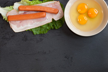 Arrangement of raw ingredients for breakfast, raw eggs, bacon, lettuce, frankfurt sausages