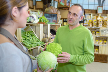 Man in greengrocers asking advice from shop assistant
