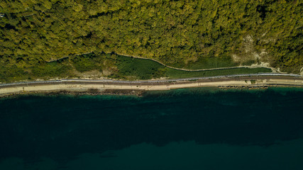 Aerial view of curvy rural road in mountains in autumn season. Cars driving below on the road.
