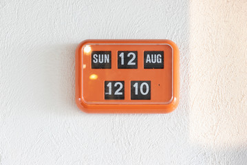 orange flip clock on white wall, retro analog timer. show time on 12 august at lunch time.