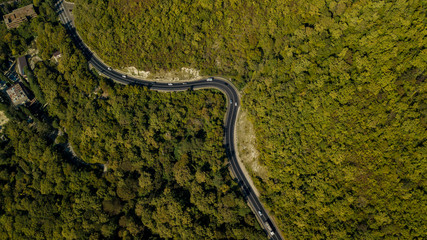 Aerial view of curvy rural road in mountains in autumn season. Cars driving below on the road.
