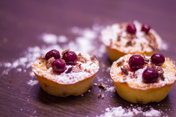 Cupcakes with cherries and powdered sugar and chocolate chips on a dark wooden background.