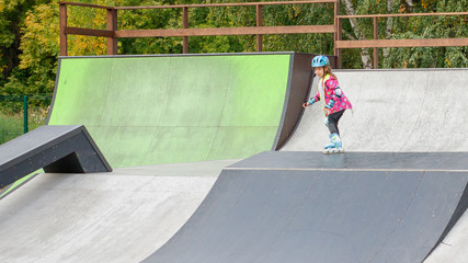 Little girl riding on roller skates in a helmet and knee pads