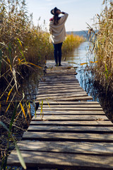 woman in a black hat and sweater stands on the old pier to the bushe