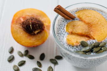 Half peach, cinnamon stick, pumpkin seeds and Chia seed pudding on wooden white table.