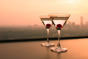 Two martini glasses on city sunset background. 