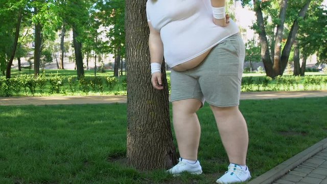 Fat man breathing heavily standing near tree, doing sports to lose weight faster