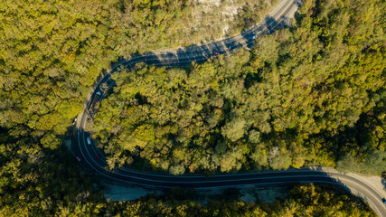 Aerial view of curvy rural road in mountains in autumn season. Cars driving below on the road.