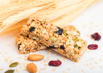 Homemade organic granola cereal bar with nuts and dried fruit on white background with oats and raw wheat.