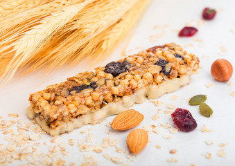 Homemade organic granola cereal bar with nuts and dried fruit on white background with oats and raw wheat.