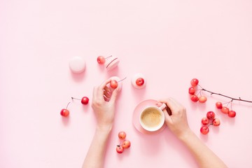 Women's hand with a cup of coffee on pink background. Pink female table with cup of cappuccino, macaroons, berries. Flat lay, top view, copy space 