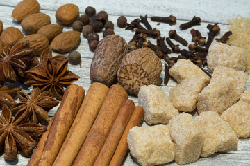 Assortment of nuts and spices, mix of various kinds of nuts, like walnut, nutmeg, pecan and almond. Cinnamon sticks and brown sugar on wooden grey background.