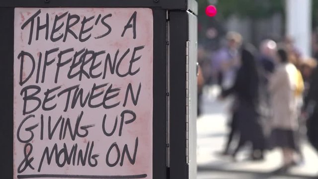 UK October 2018 - Out of focus people on a street walk past a homemade fly poster sign on an electrical junction box that says, &sbquo;&Auml;&uacute;There&sbquo;&Auml;&ocirc;s a difference between giving up and moving on&sbquo;&Auml;&ugrave;.