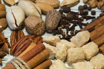 Assortment of nuts and spices, mix of various kinds of nuts, like walnut, nutmeg, pecan and almond. Cinnamon sticks and brown sugar on wooden grey background.