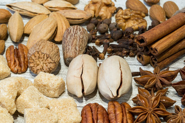 Assortment of nuts and spices, mix of various kinds of nuts, like walnut, nutmeg, pecan and almond. Cinnamon sticks and brown sugar on wooden grey background.