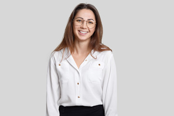 Indoor shot of pleasant looking smiling young female architect wears transparent round glasses,...