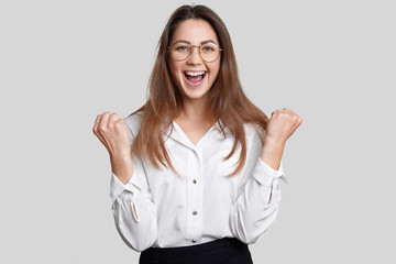 Overjoyed student wears elegant clothes, clenches fists with happiness, rejoices successfully...