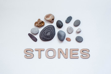 Beautiful sea stones of different sizes and colors, isolated and laid out on a light stylish background. Next to the inscription from the wooden letters 
