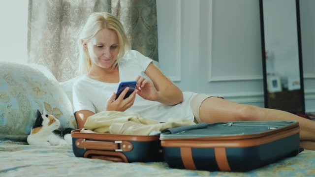 A woman going on vacation. Uses a smartphone around a half-packed travel bag