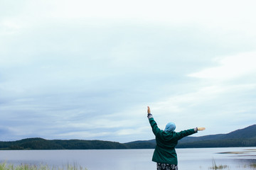 muslim woman stands raising her arms overlooking the mountains and the lake