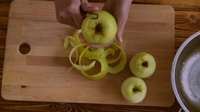 Woman is peeling green aples on the kitchen, top view