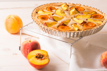Open pie with peaches in almond cream on a white wooden background. Delicious and sweet peach tart