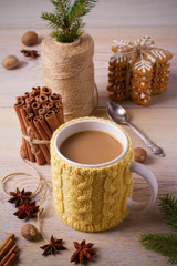 Knitted yellow cup with hot winter drink, cookies, cinnamon, decorations. Cozy