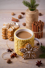 Knitted yellow cup with hot winter drink, cookies, cinnamon, decorations. Cozy