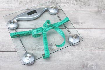 Bow of a green tape measure around glass weighing scale on a rustic surface with copy space
